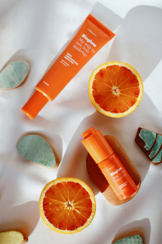 Orange skincare tubes and halved oranges on a white surface with decorative stones